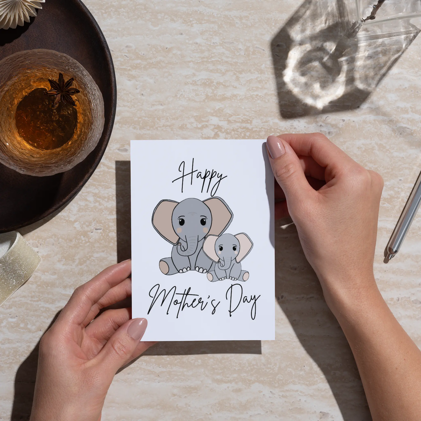 Person holding a Mother's Day card with elephant illustrations on a table.