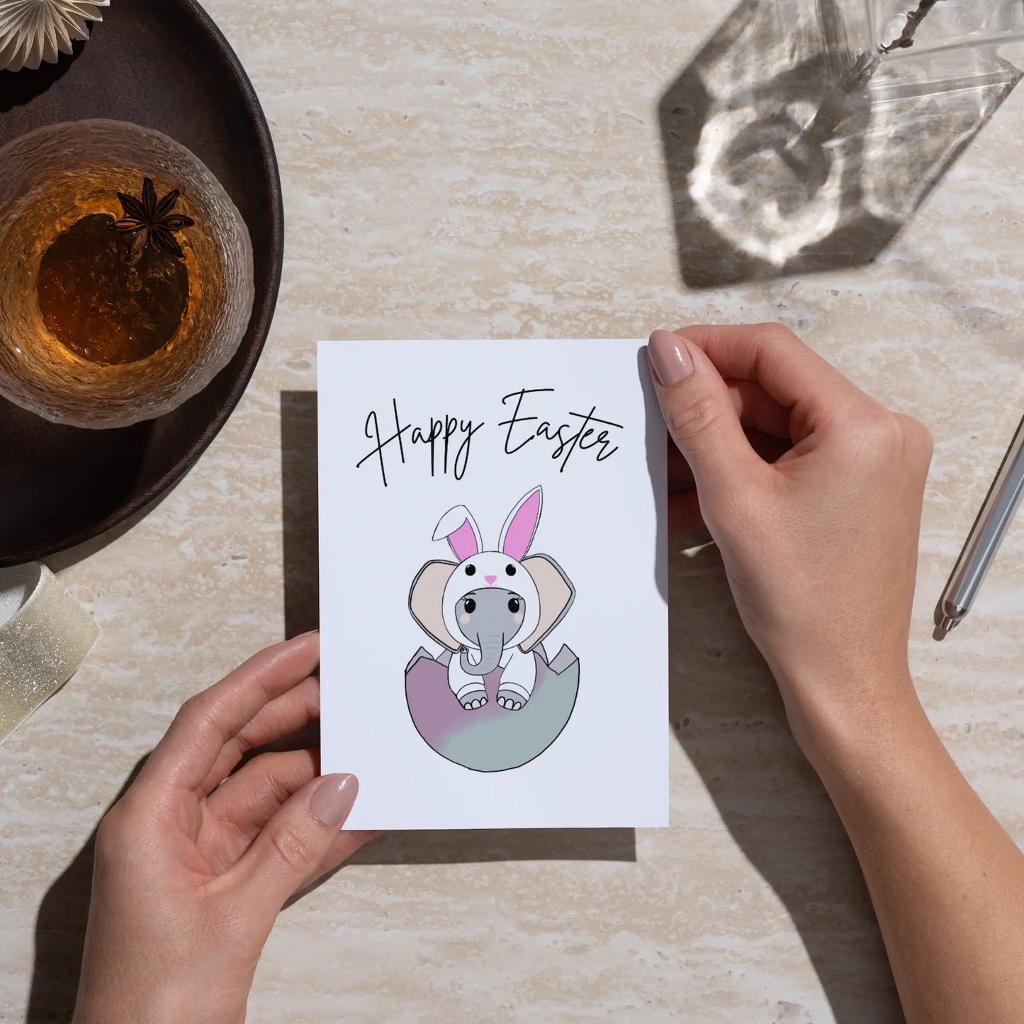 Person holding a 'Happy Easter' card with an elephant wearing bunny ears on a table.