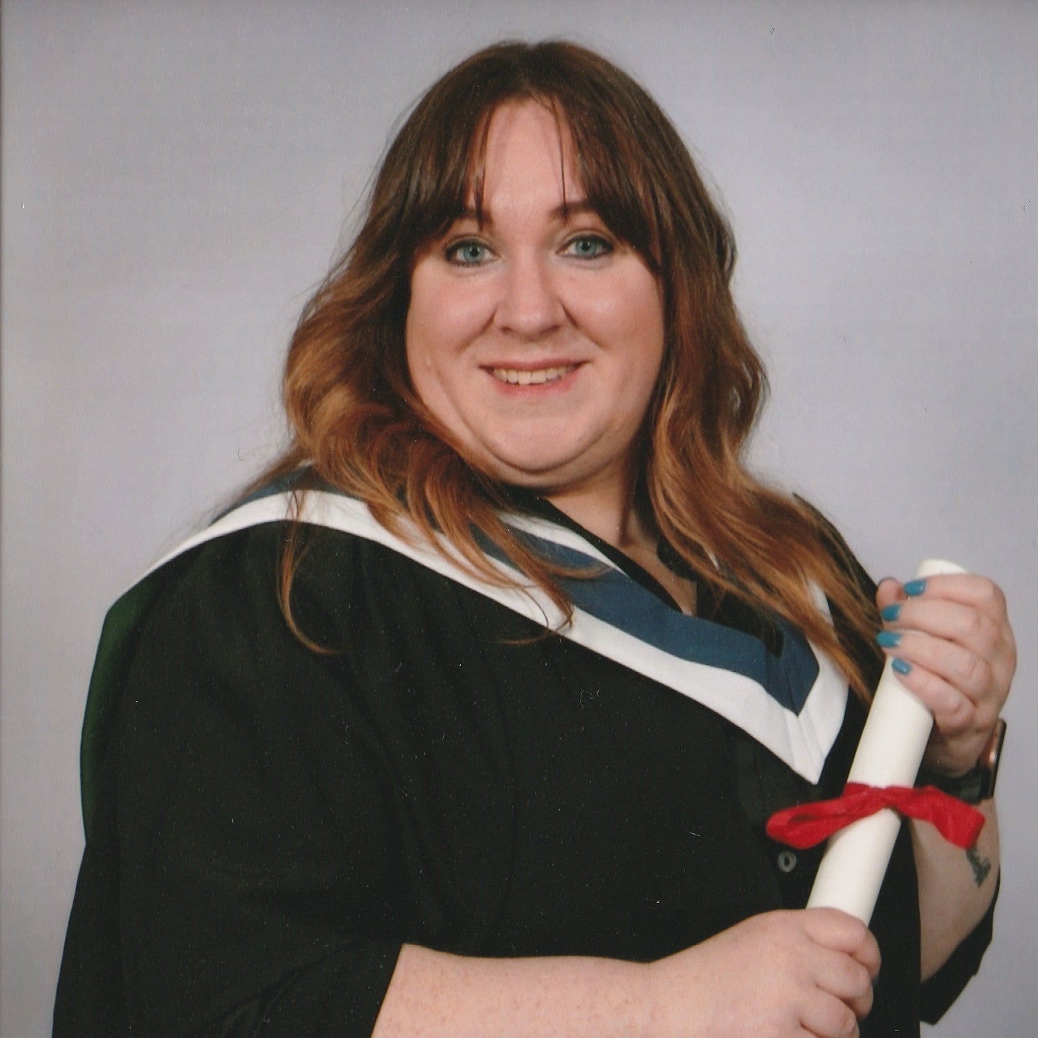 Lisa is wearing her graduation gown in the Queen Margaret University Masters colours holding a certificate.